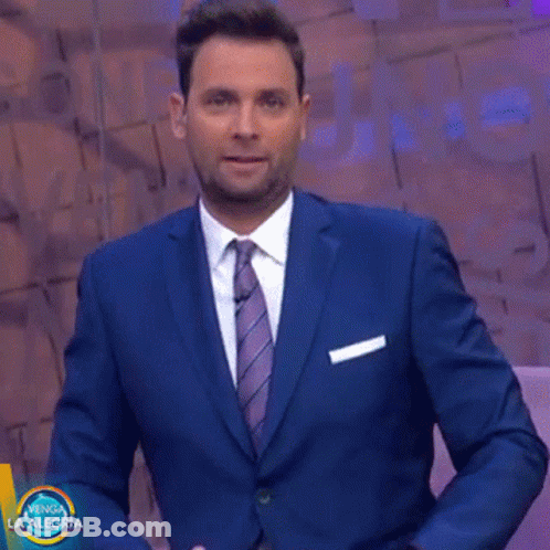 A Man In A Suit And Tie Stands In Front Of A Sign That Says " Venga La Alegria " GIF
