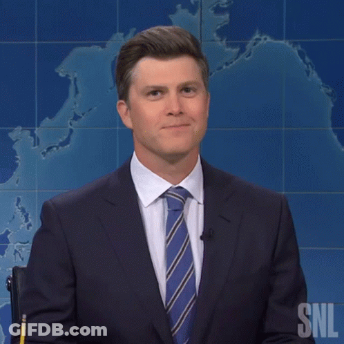 A Man In A Suit And Tie Stands In Front Of A Snl Poster GIF