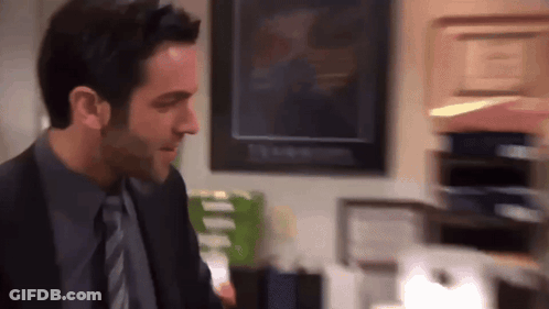 A Man In A Suit And Tie Stands In Front Of A Stack Of Papers GIF