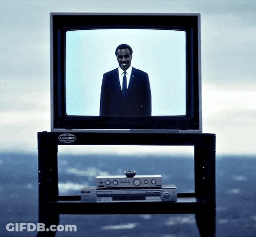 A Man In A Suit And Tie Stands In Front Of A Television That Says Lumin On It GIF