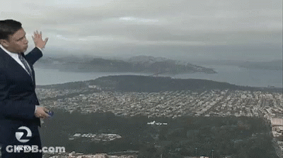 A Man In A Suit And Tie Stands In Front Of A View Of A City And Mountains With The Number 2 On His Shirt GIF