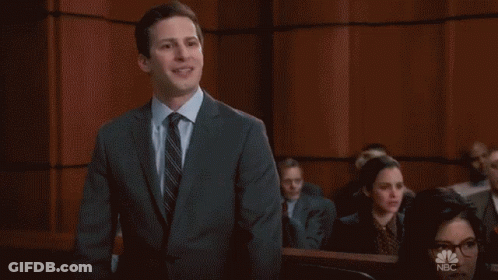 A Man In A Suit And Tie Stands In Front Of A Wall That Says Cool On It GIF