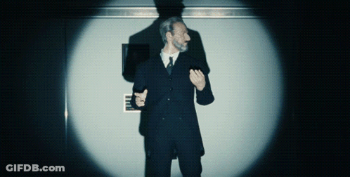 A Man In A Suit And Tie Stands In Front Of A Wall With A Sign That Says ' Emergency Exit ' On It GIF