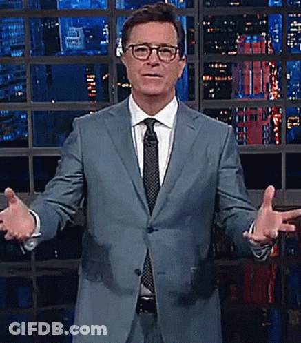 A Man In A Suit And Tie Stands In Front Of A Window GIF
