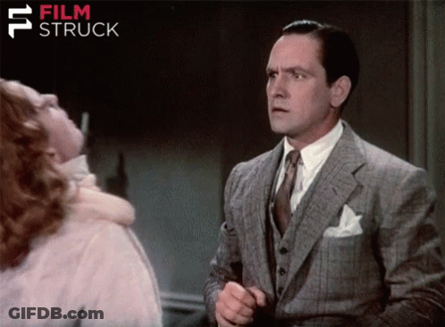 A Man In A Suit And Tie Stands In Front Of A Woman With Film Struck Written In The Corner GIF