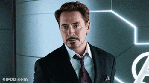 A Man In A Suit And Tie Stands In Front Of An Avengers Sign GIF