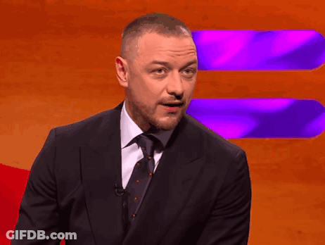 A Man In A Suit And Tie Stands In Front Of An Orange And Purple Background GIF