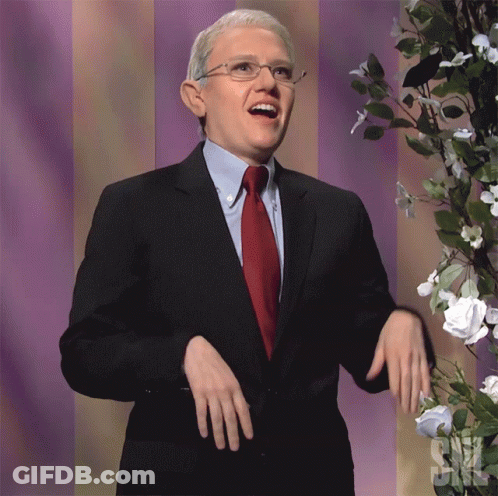 A Man In A Suit And Tie Stands In Front Of Flowers And A Sign That Says ' Snl ' GIF