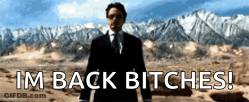 A Man In A Suit And Tie Stands In Front Of Mountains And Says I 'M Back Bitches ! GIF