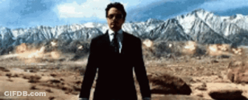 A Man In A Suit And Tie Stands In Front Of Mountains GIF