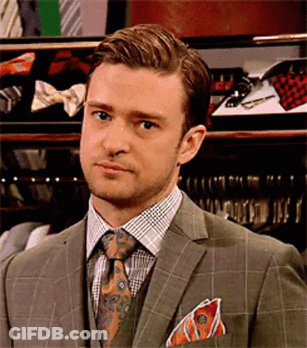 A Man In A Suit And Tie Stands In Front Of Tie Racks GIF