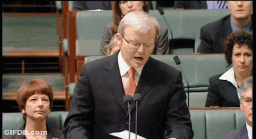 A Man In A Suit And Tie Stands In Front Of Two Microphones GIF