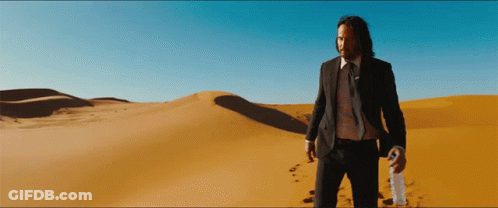 A Man In A Suit And Tie Stands In The Desert Holding A Bottle GIF