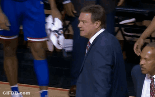 A Man In A Suit And Tie Stands Next To A Basketball Player Holding His Shoes GIF