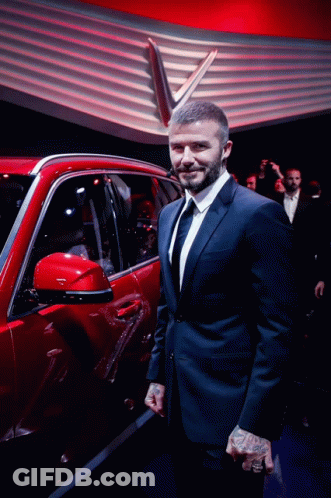 A Man In A Suit And Tie Stands Next To A Red Car GIF