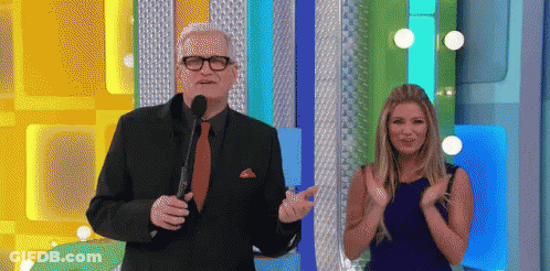 A Man In A Suit And Tie Stands Next To A Woman In A Blue Dress Who Is Clapping GIF