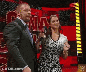 A Man In A Suit And Tie Stands Next To A Woman In A Leopard Print Dress Holding A Microphone .. GIF