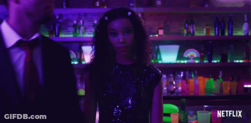 A Man In A Suit And Tie Stands Next To A Woman In A Sequined Dress In Front Of A Netflix Logo GIF
