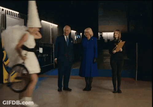 A Man In A Suit And Tie Stands Next To A Woman In A White Dress And A Woman In A Blue Coat GIF