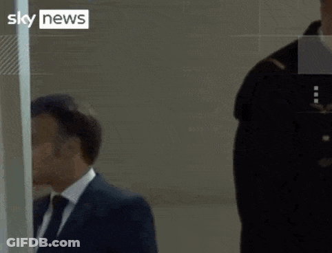 A Man In A Suit And Tie Stands Next To A Woman In A Yellow Vest That Says Sky News GIF