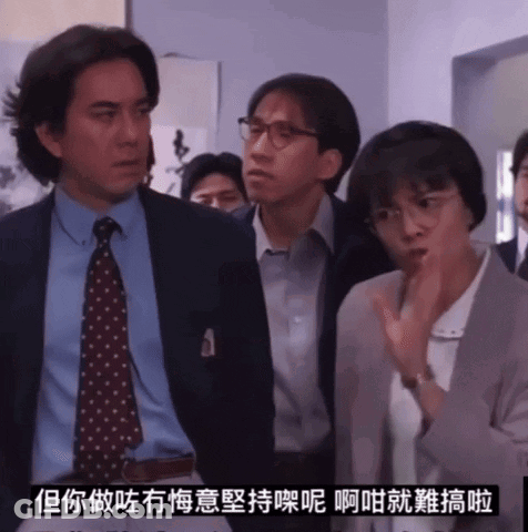 A Man In A Suit And Tie Stands Next To A Woman In Glasses GIF