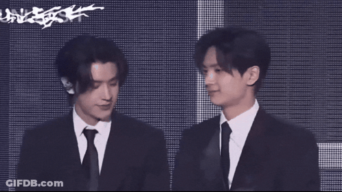 A Man In A Suit And Tie Stands Next To Another Man GIF