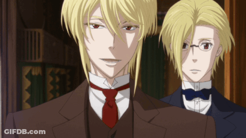 A Man In A Suit And Tie Stands Next To Another Man In A Tuxedo GIF