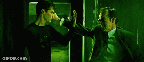 A Man In A Suit And Tie Stands Next To Another Man GIF