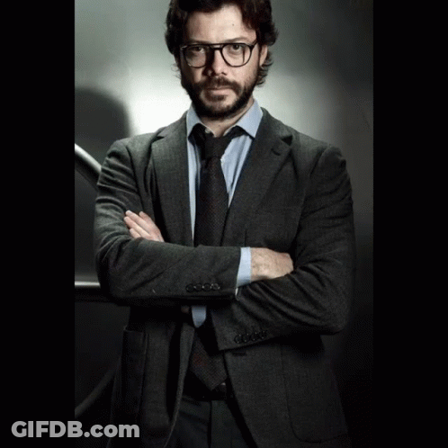 A Man In A Suit And Tie Stands With His Arms Crossed In Front Of A Vault Door GIF