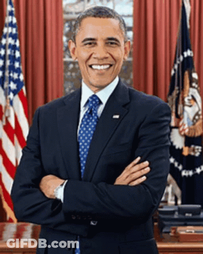 A Man In A Suit And Tie Stands With His Arms Crossed In Front Of An American Flag GIF