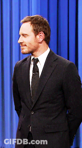 A Man In A Suit And Tie Stands With His Hands Behind His Back GIF