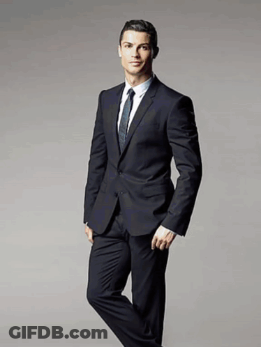 A Man In A Suit And Tie Stands With His Leg Crossed GIF