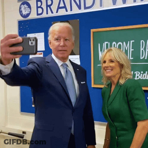Man In Suit And Woman In Green Suit Taking Selfie GIF