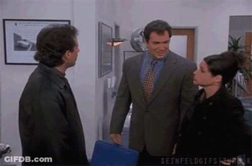 A Man In A Suit And Tie Talks To A Woman In A Black Jacket GIF