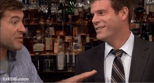 A Man In A Suit And Tie Talks To Another Man In A Bar GIF