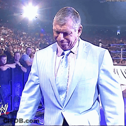 A Man In A Suit And Tie Walks Into A Wrestling Ring With The Letters W On The Bottom Right GIF
