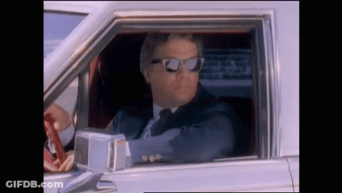 A Man In A Suit And Tie Wearing Sunglasses Is Driving A Car GIF