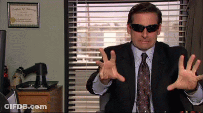 A Man In A Suit And Tie Wearing Sunglasses Is Sitting In Front Of A Window GIF