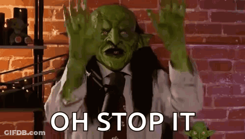 A Man In A Suit And Tie With A Green Mask On His Face Is Making A Stop Sign . GIF