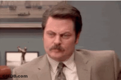 A Man In A Suit And Tie With A Mustache Is Sitting At A Desk . GIF