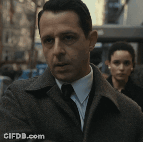 A Man In A Suit And Tie With A Woman In The Background GIF