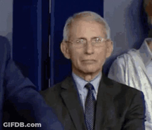 A Man In A Suit And Tie With Glasses Is Standing In Front Of A Blue Wall . GIF