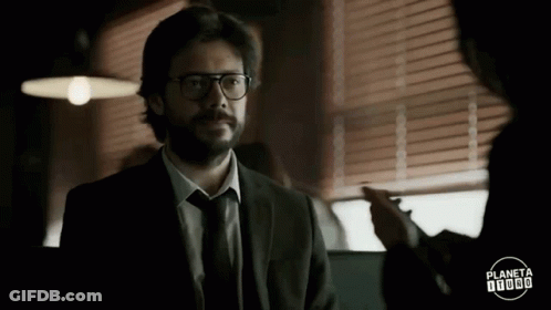 A Man In A Suit And Tie With Glasses Is Talking To Another Man . GIF