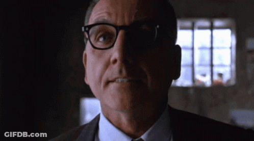 A Man In A Suit And Tie With Glasses Looks At The Camera GIF
