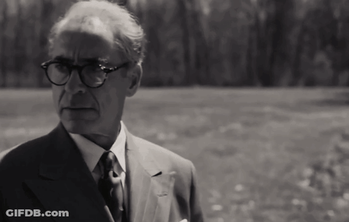 A Man In A Suit And Tie With Glasses Stands In A Field GIF