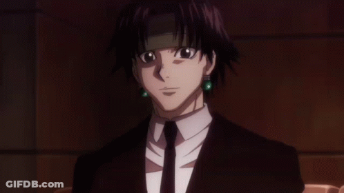 A Man In A Suit And Tie With Green Earrings Looks At The Camera GIF