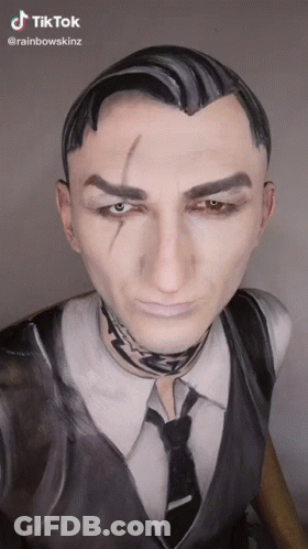 A Man In A Suit And Tie With His Face Painted . GIF