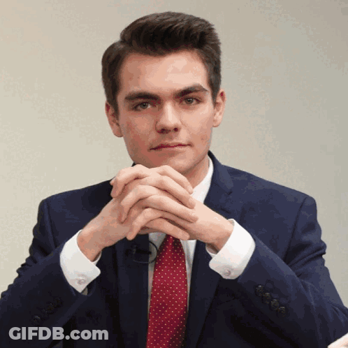 A Man In A Suit And Tie With His Hands Folded In Front Of His Face GIF
