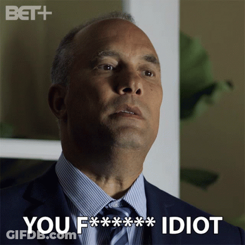 A Man In A Suit And Tie With The Words You F *** Idiot Above Him GIF