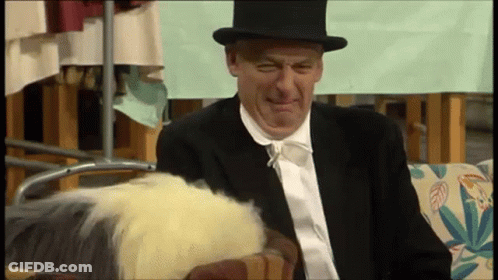 A Man In A Suit And Top Hat Is Sitting On A Couch . GIF